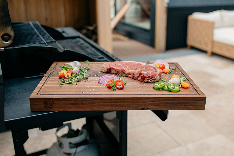 meat on a cutting board next to a grill